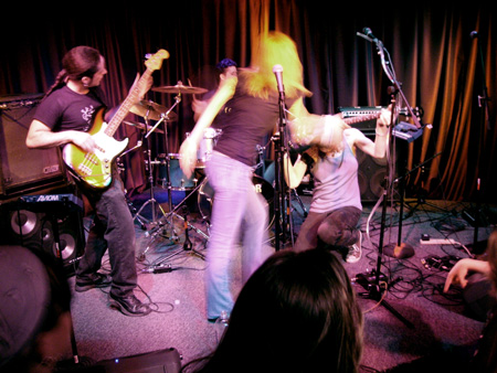 Mobius Donut playing live in Walnut Creek. Kevin on the left playing bass. Cindy Lou from behind strumming Andrea's guitar. Andrea is on her knees holding up the guitar to strum