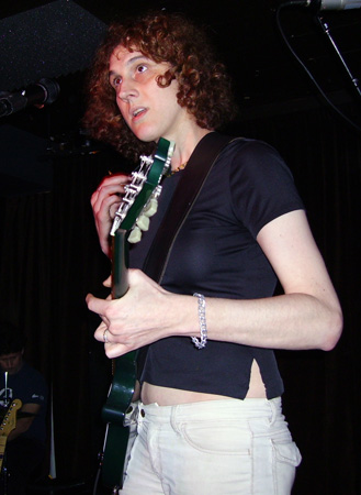 Adrea Hensler playing guitar against a black background